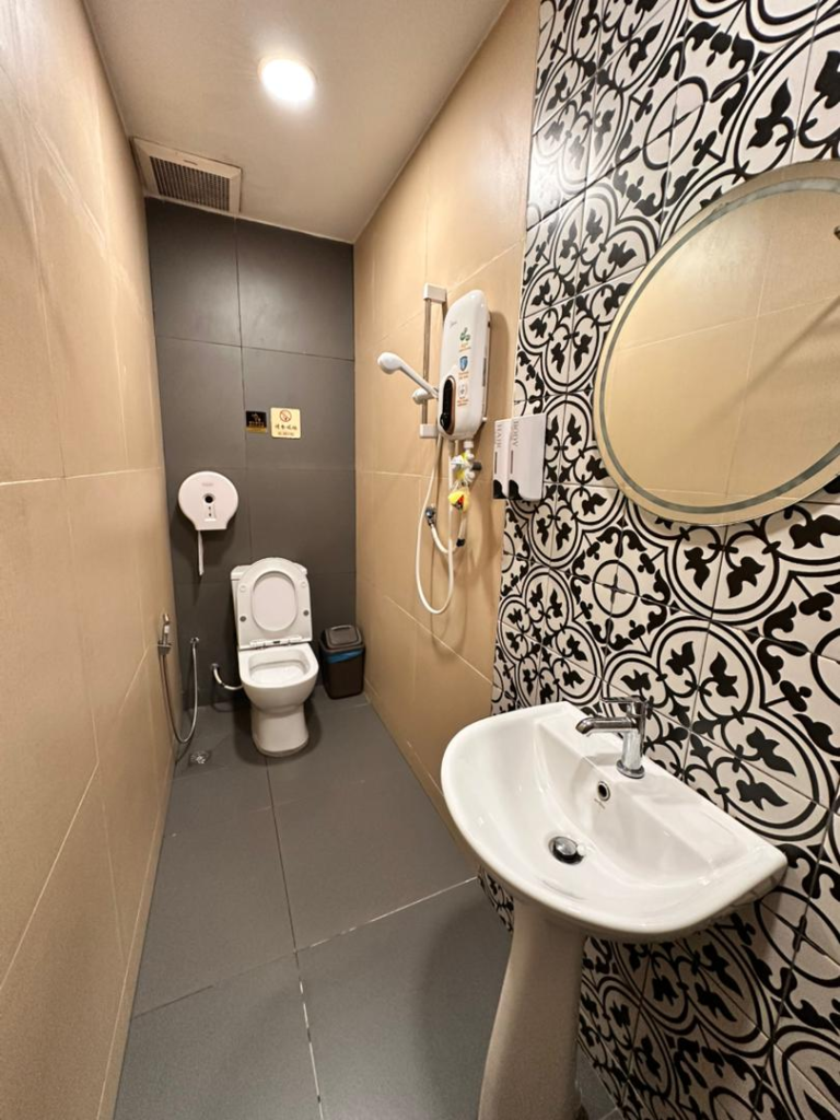 Narrow bathroom with a toilet at the far end, pedestal sink on the right, and black‑and‑white patterned wall tiles by the mirror.
